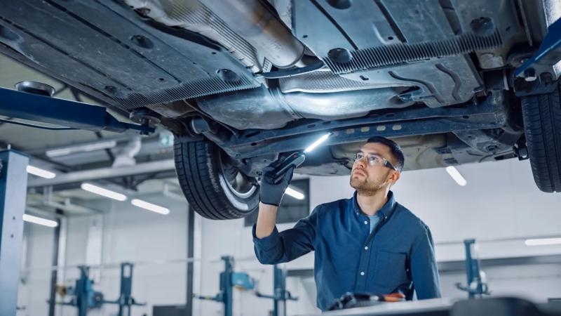 COLOUR-IMAGE_automotive-male-mechanic-shining-light-inspecting-under-car_feb26
