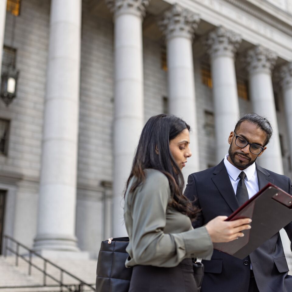 COLOUR-IMAGE_man-and-woman-looking-at-documents-in-front-of-government-building_feb26