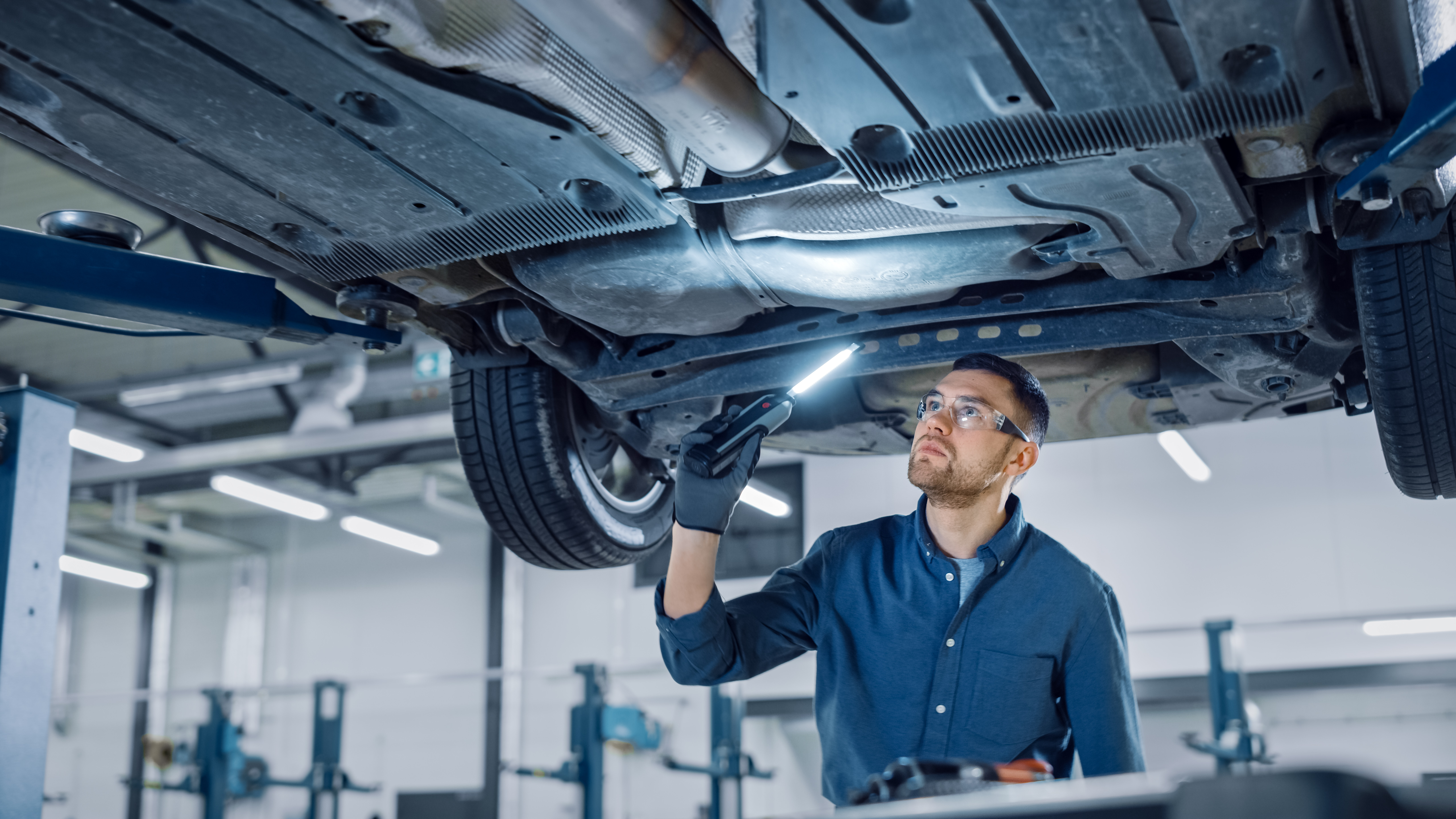 COLOUR-IMAGE_automotive-male-mechanic-shining-light-inspecting-under-car_feb26