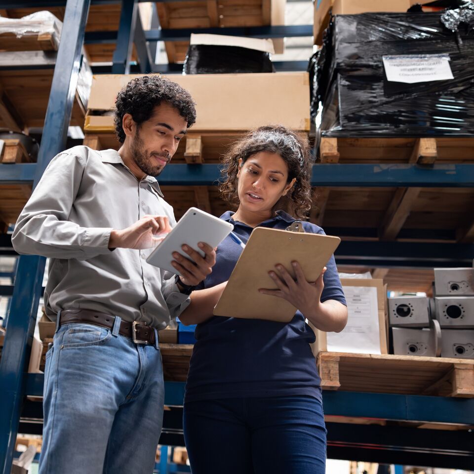 COLOUR-IMAGE_man-and-woman-in-factory-looking-at-tablet-and-clipboard_apr26